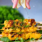 Lemon wedge being squeezed over Persian joojeh kabob (saffron chicken) with flatbread and rocket.