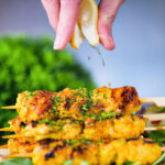 Lemon wedge being squeezed over Persian joojeh kabob (saffron chicken skewers).