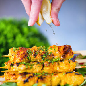 Lemon wedge being squeezed over Persian joojeh kabob (saffron chicken skewers).