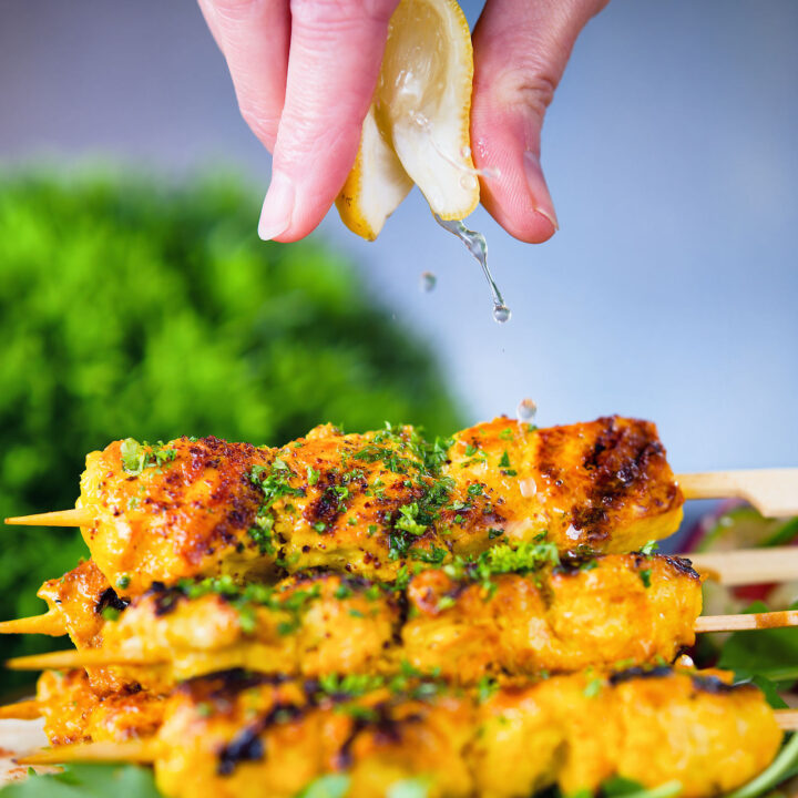 Lemon wedge being squeezed over Persian joojeh kabob (saffron chicken skewers).