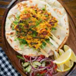 Overhead Persian joojeh kabob (saffron chicken skewers) with flatbread, Shirazi salad and lemon wedges.