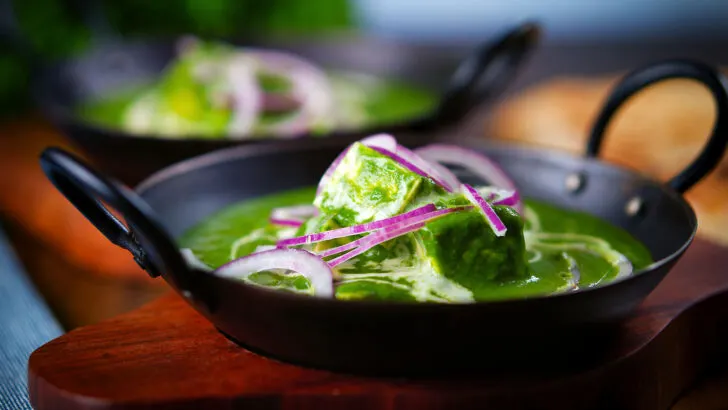 Palak paneer, Indian spinach and cheese curry garnished with red onion and cream.