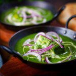 Palak paneer, Indian spinach and cheese curry garnished with red onion and cream.