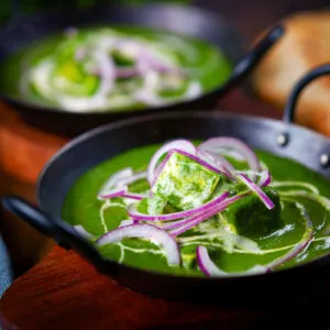 Palak paneer, Indian spinach and cheese curry garnished with red onion and cream.