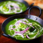 Palak paneer, Indian spinach curry garnished with red onion and cream served with naan bread.