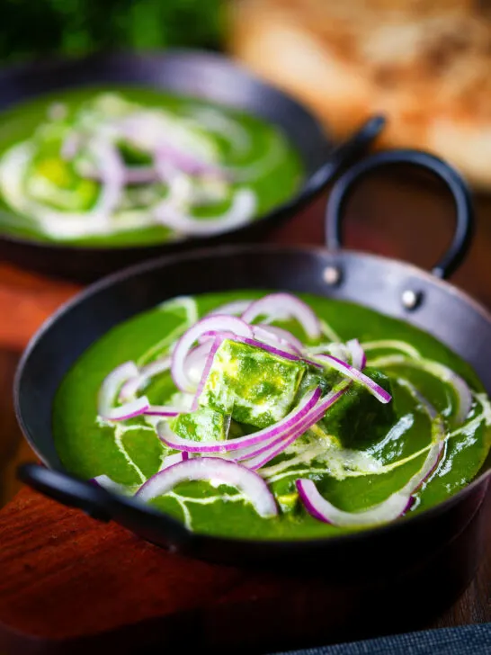 Palak paneer, Indian spinach curry garnished with red onion and cream served with naan bread.