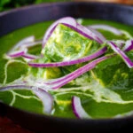 Close-up palak paneer, Indian spinach curry garnished with red onion and cream.