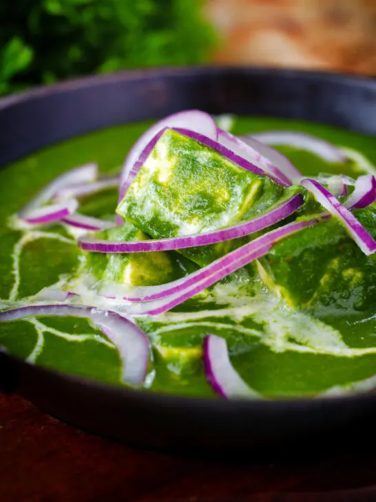 Close-up palak paneer, Indian spinach curry garnished with red onion and cream.