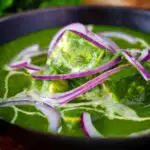 Close-up palak paneer, Indian spinach curry garnished with red onion and cream.