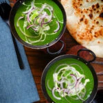 Overhead palak paneer, Indian spinach curry garnished with red onion and cream served with naan bread.