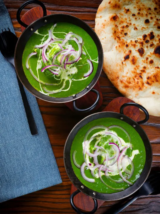 Overhead palak paneer, Indian spinach curry garnished with red onion and cream served with naan bread.