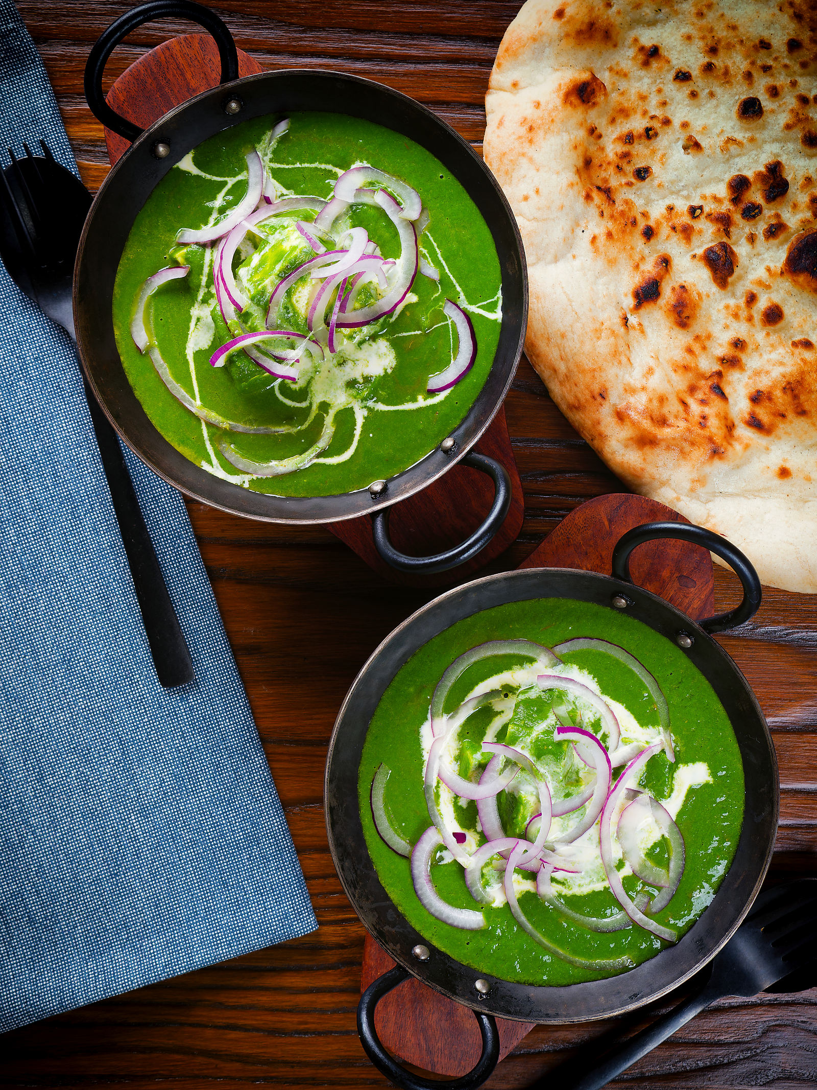 Overhead palak paneer, Indian spinach curry garnished with red onion and cream served with naan bread.