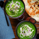 Overhead palak paneer, Indian spinach curry garnished with red onion and cream served with naan bread.