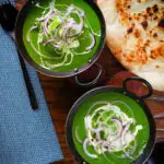 Overhead palak paneer, Indian spinach curry garnished with red onion and cream served with naan bread.