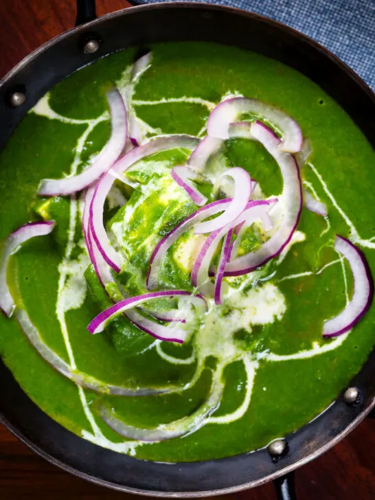 Close-up overhead palak paneer, Indian spinach curry garnished with red onion and cream.