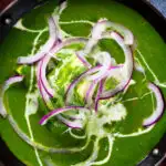 Close-up overhead palak paneer, Indian spinach curry garnished with red onion and cream.
