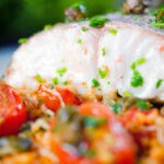 Close-up oven roasted hake with cherry tomatoes and capers served with pourgori.