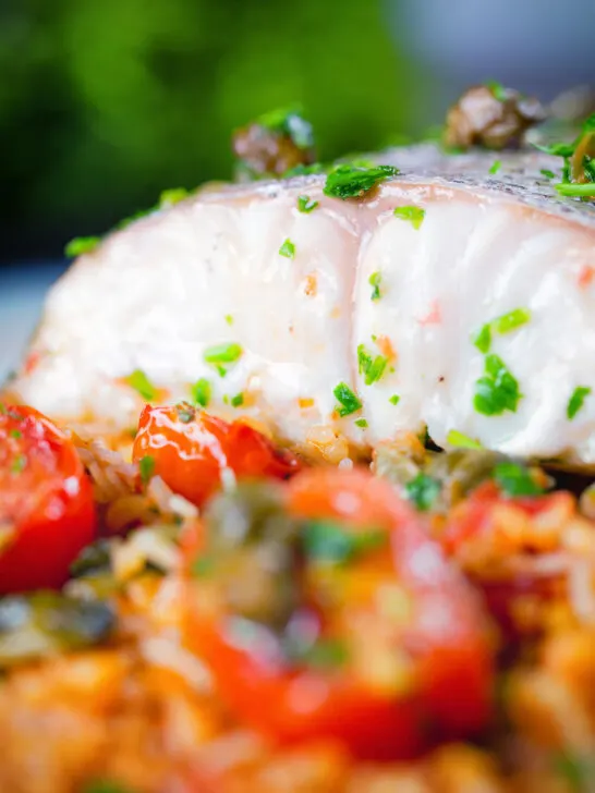 Close-up oven roasted hake with cherry tomatoes and capers served with pourgouri.