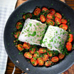 Oven roasted hake fillet with cherry tomatoes, capers and parsley.