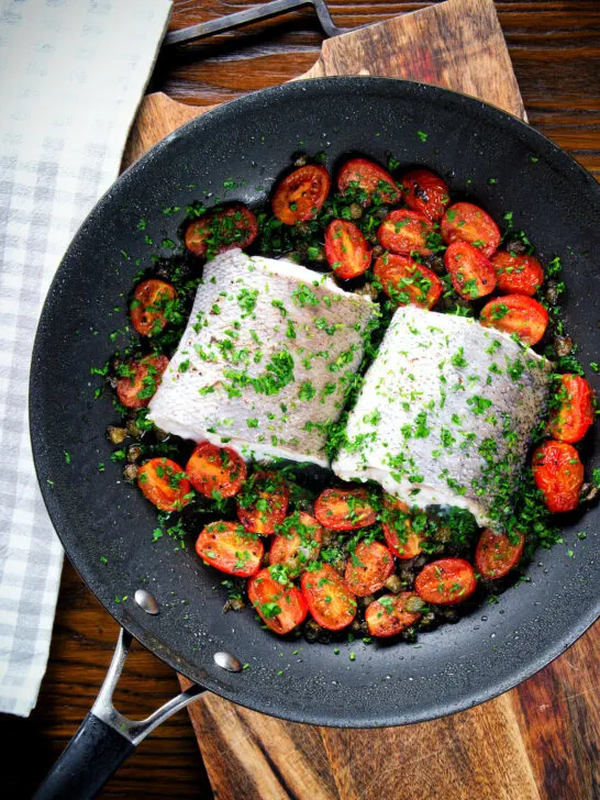 Oven roasted hake fillet with cherry tomatoes, capers and parsley.