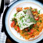 Overhead oven roasted hake with cherry tomatoes and capers served with pourgori.