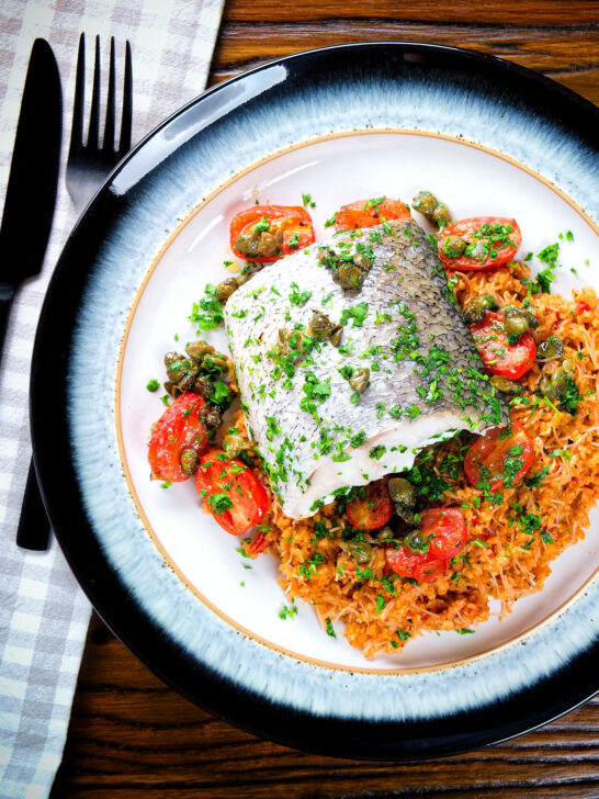 Overhead oven roasted hake with cherry tomatoes and capers served with pourgouri.