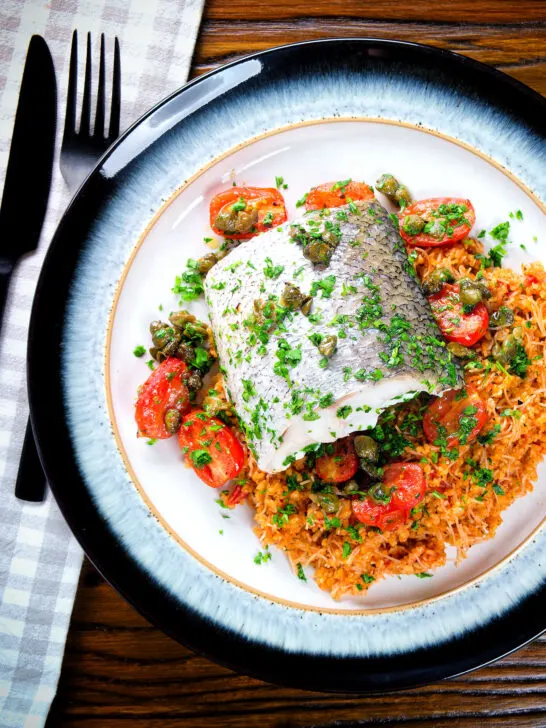 Overhead oven roasted hake with cherry tomatoes and capers served with pourgouri.
