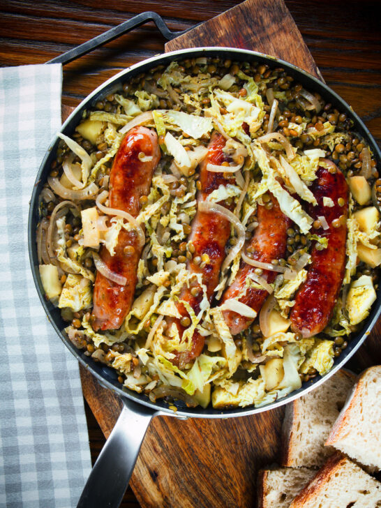 Overhead sausage and lentil stew with cabbage, apples and English mustard served in its cooking pot.