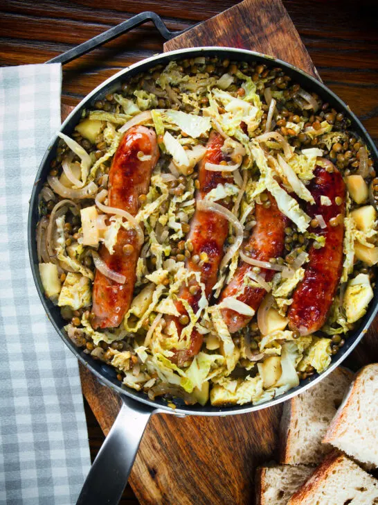 Overhead sausage and lentil stew with cabbage, apples and English mustard served in its cooking pot.