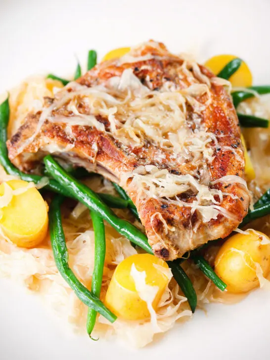 Close-up slow cooker pork chops and sauerkraut with potatoes and green beans.