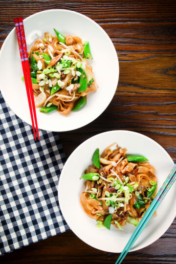 Overhead ho fun noodles stir fry with bean sprouts, shiitake mushrooms and sugar snap peas.