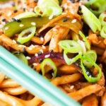 Close up stir fried teriyaki chicken noodles with spring onions and sesame seeds.