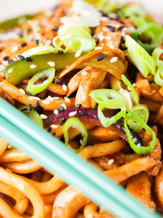 Close up stir fried teriyaki chicken noodles with spring onions and sesame seeds.