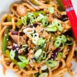 Close-up overhead stir fried teriyaki chicken noodles with spring onions and sesame seeds.
