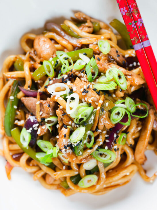 Close-up overhead stir fried teriyaki chicken noodles with spring onions and sesame seeds.