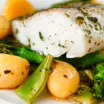 Close-up cod traybake with potatoes, broccoli and runner beans cooked in a herby olive oil.