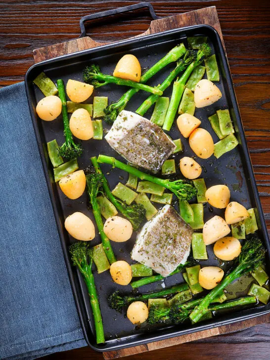 Overhead cod traybake with potatoes, broccoli and runner beans on a sheet pan.