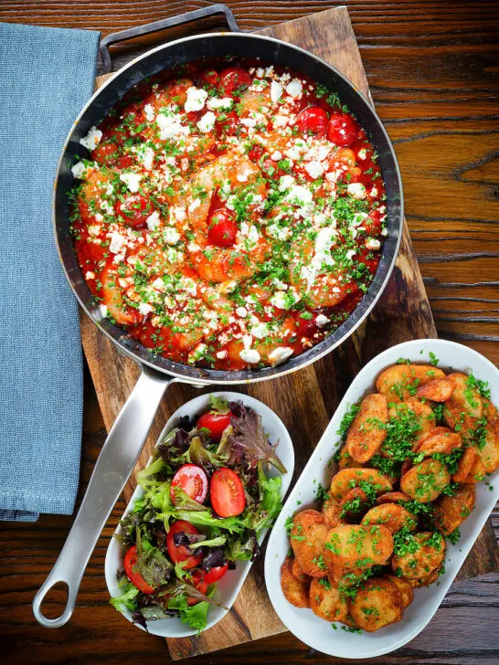 Overhead Greek prawn (shrimp) saganaki with feta cheese served with potatoes and salad.