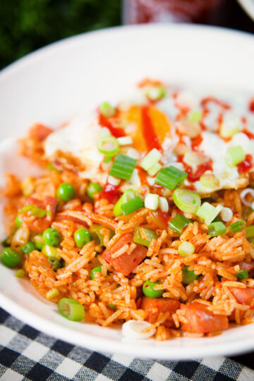 Spicy Spam fried rice with kimchi and peas, served with a fried egg and Sriracha sauce.