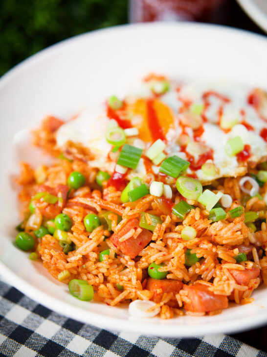 Spicy Spam fried rice with kimchi and peas, served with a fried egg and Sriracha sauce.
