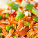 Close-up spicy Spam fried rice with kimchi and peas, served with a fried egg and Sriracha sauce.