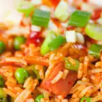 Close-up spicy Spam fried rice with kimchi and peas, served with a fried egg and Sriracha sauce.