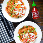 Overhead spicy Spam fried rice with kimchi and peas, served with a fried egg and Sriracha sauce.