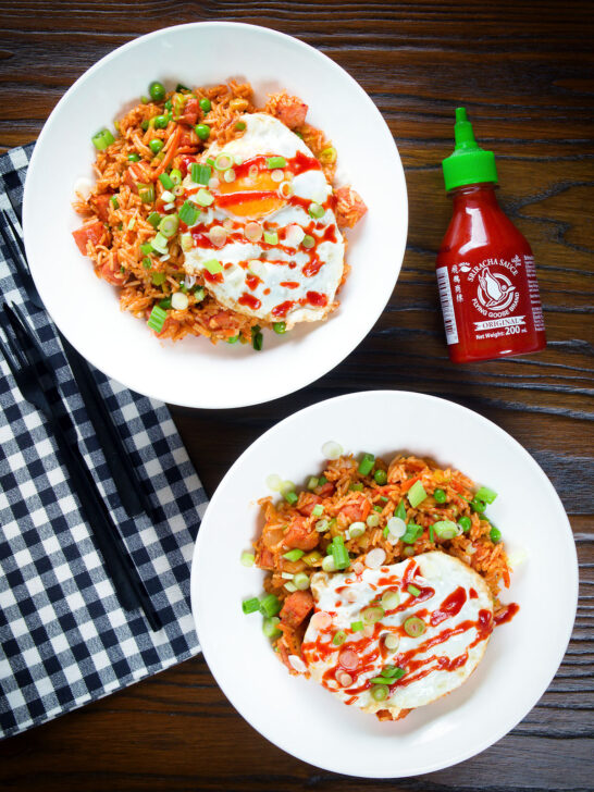 Overhead spicy Spam fried rice with kimchi and peas, served with a fried egg and Sriracha sauce.
