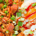 Close-up overhead spicy Spam fried rice with kimchi and peas, served with a fried egg and Sriracha sauce.
