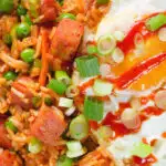 Close-up overhead spicy Spam fried rice with kimchi and peas, served with a fried egg and Sriracha sauce.