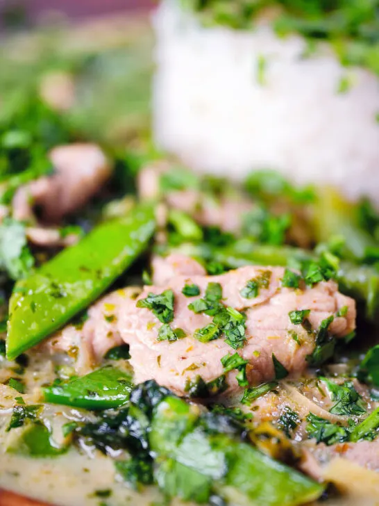 Close-up herby Thai green pork curry with sugar snap peas and jasmine rice.