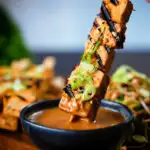 Tofu satay skewers being dipped into a homemade peanut dipping sauce.