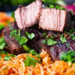 Close-up Afelia or Cypriot pork braised in red wine and coriander seeds showing meat texture served with pourgouri.