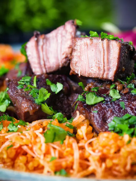 Close-up Afelia or Cypriot pork braised in red wine and coriander seeds showing meat texture served with pourgouri.